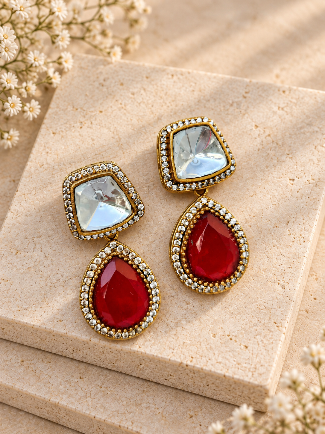 Adaa red teardrop earrings with irregular clear square tops and gold-tone borders on beige square stones.