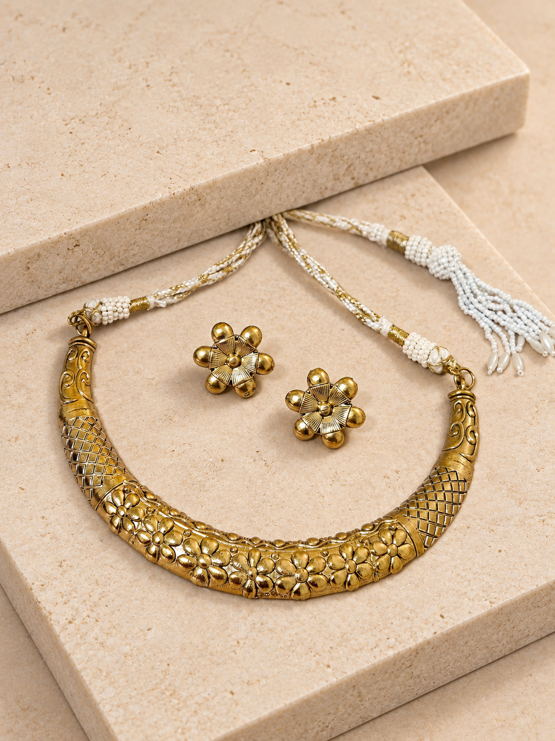 Antique gold-tone floral Hasli necklace with matching flower studs and white cord on beige square stones.