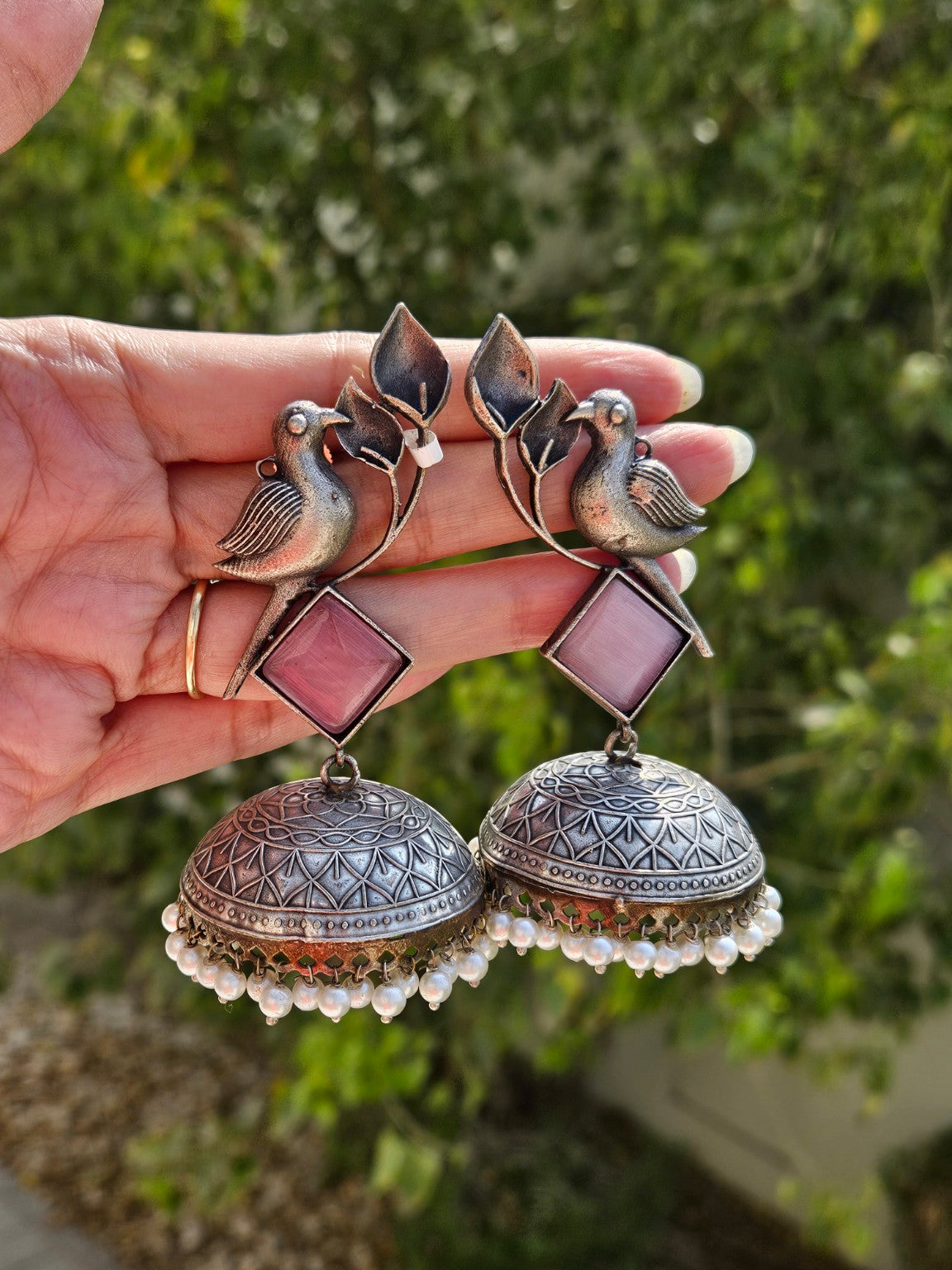 Bird motif pink stone oxidized silver jhumka earrings in natural daylight