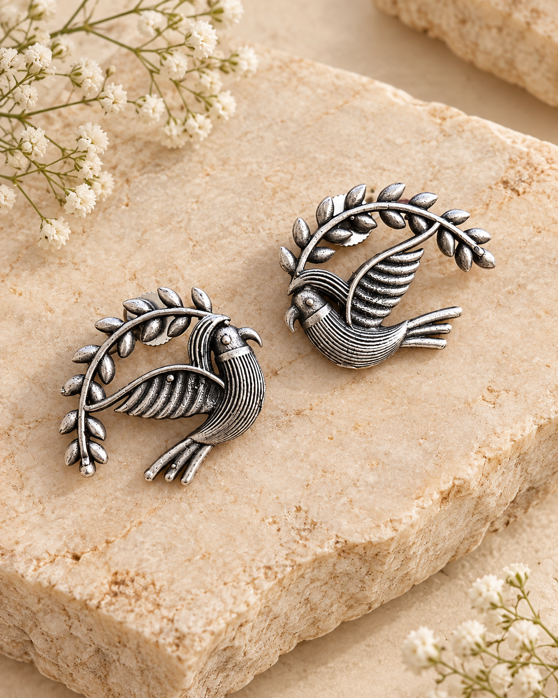 Silver lookalike bird earrings on beige stone background