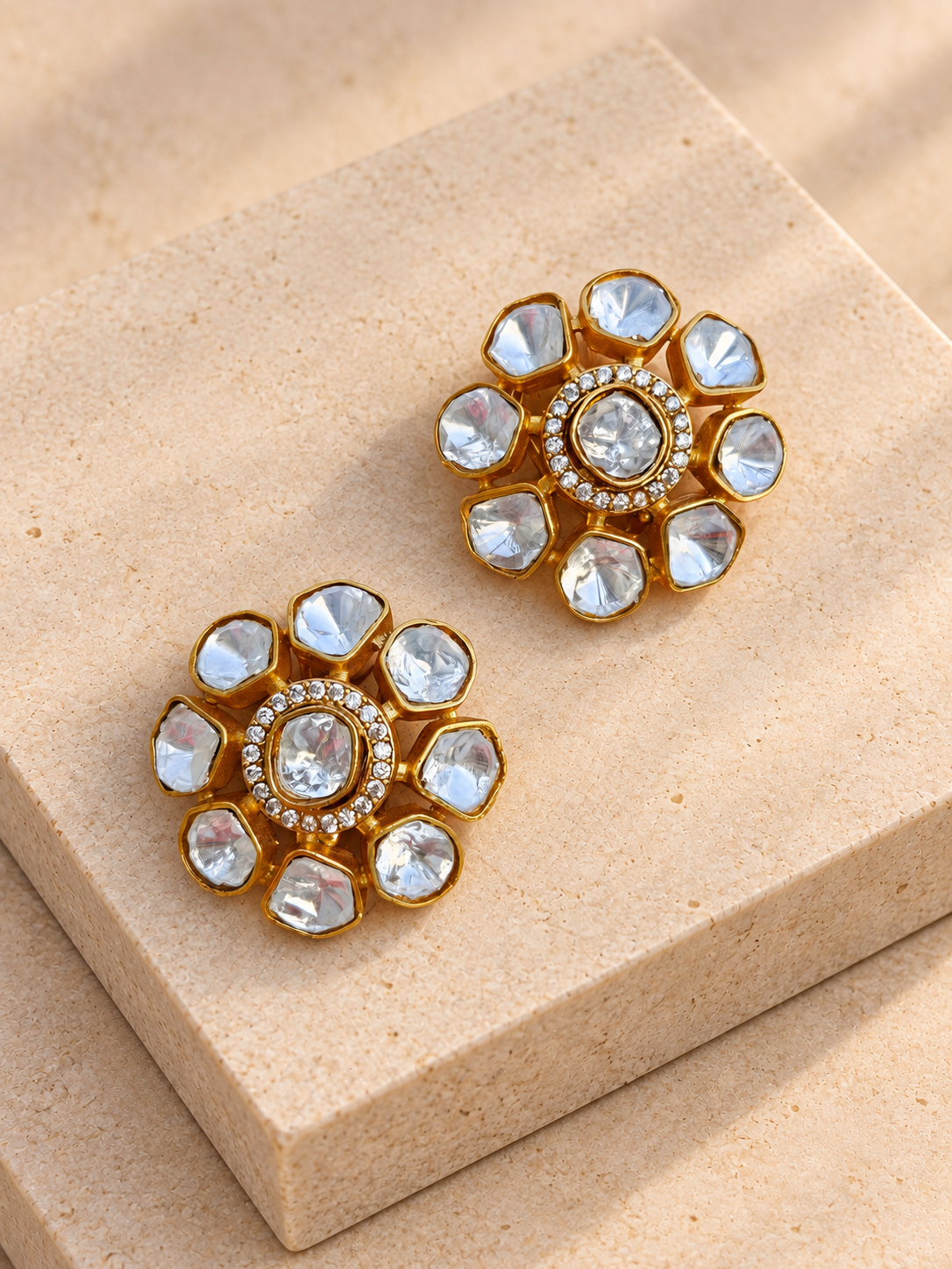 Clear irregular-petal flower stud earrings resting directly on beige square stones.
