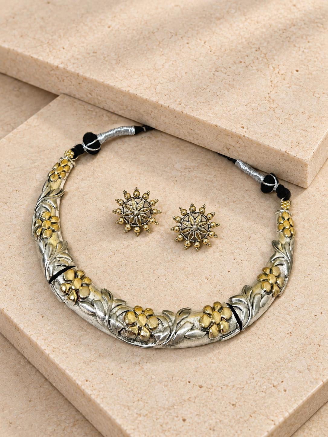 Dual-tone floral Hasli necklace and matching round studs resting on beige square stones.