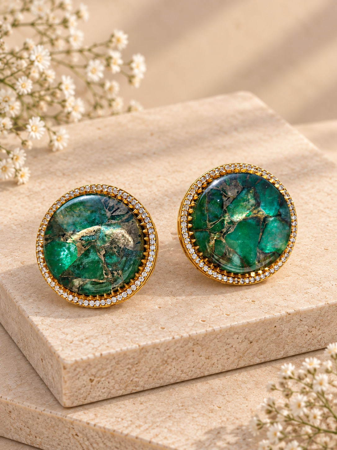 Round green doublet stud earrings with irregular gold-toned veining and clear-stone borders on beige square stones.