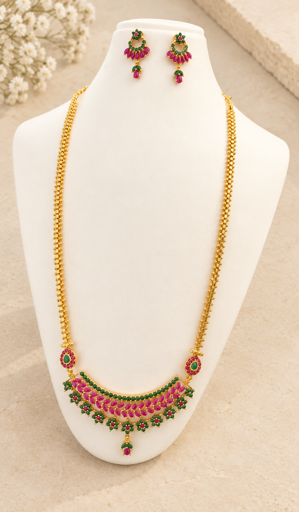 Gold-tone long necklace and matching pink-and-green stone earrings displayed against beige stone.