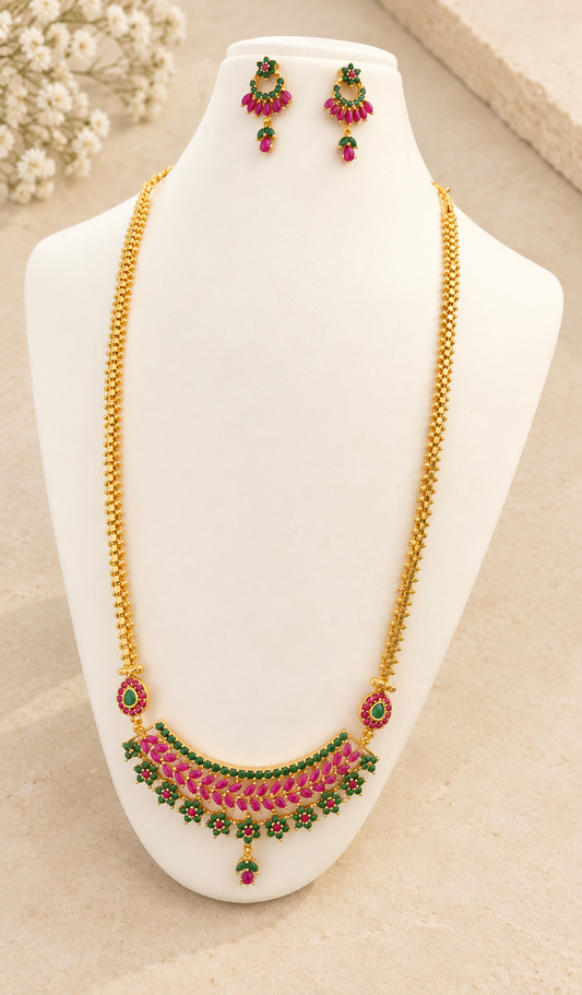 Gold-tone long necklace and matching pink-and-green stone earrings displayed against beige stone.