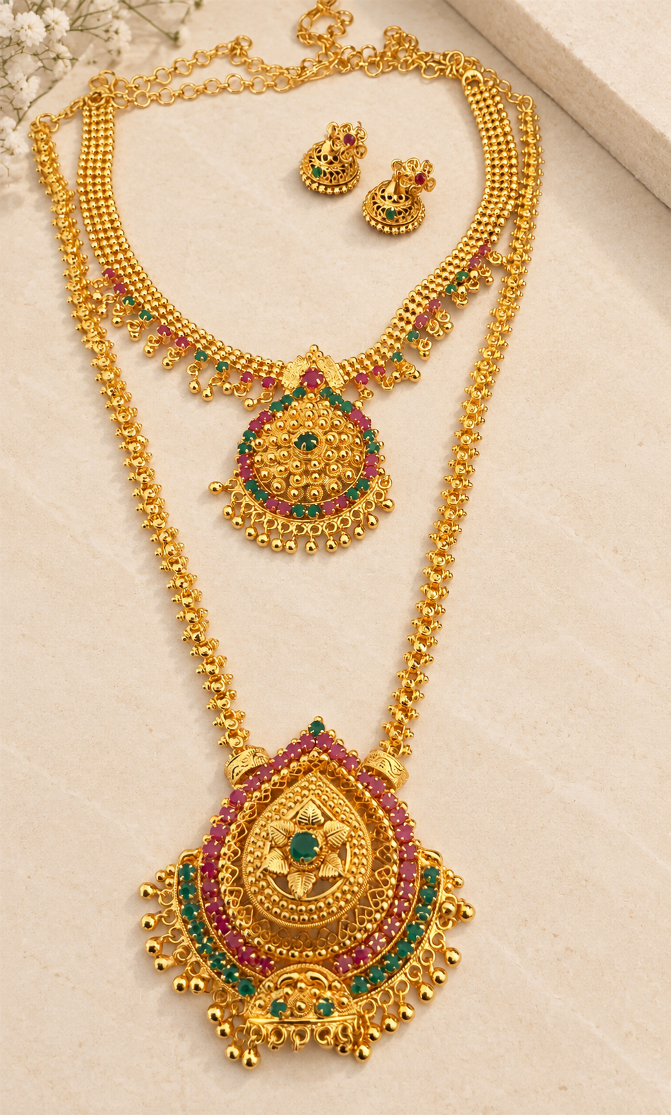 Gold-tone long and short necklaces with pink and green stones and matching earrings on beige stone.
