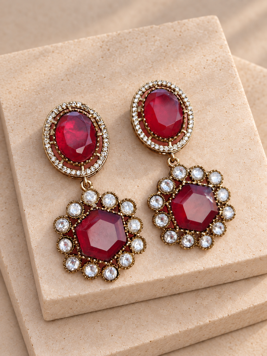 Noor red oval and hexagonal drop earrings with clear-stone borders on beige square stones.