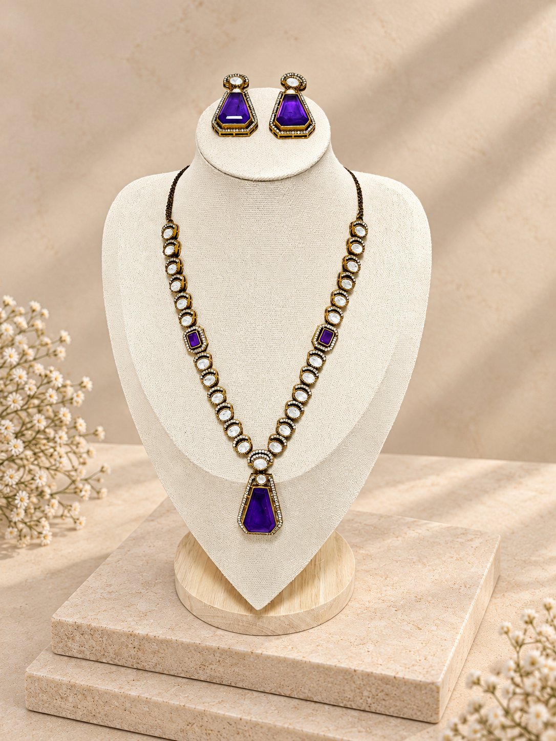 Purple pendant necklace and matching earrings displayed on a cream bust above two beige square stones.