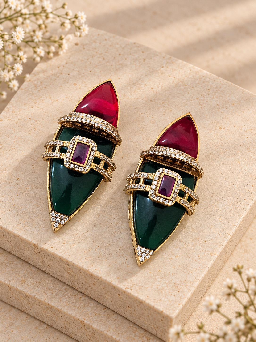 Red and dark green pointed earrings with purple rectangular centre stones on two beige square stones.