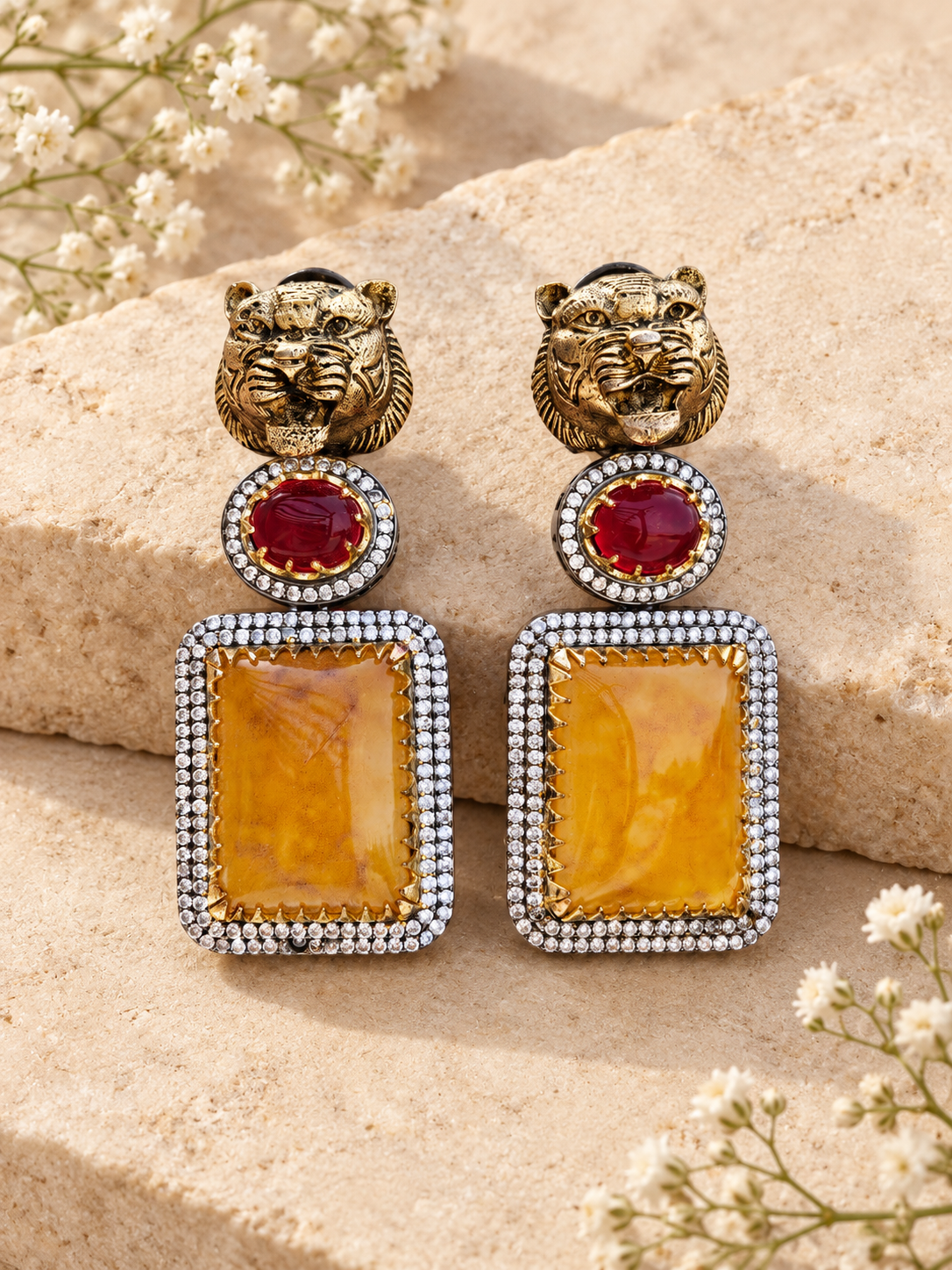 Sabya-inspired lightweight tiger head statement earrings with red and amber stones on beige stone background