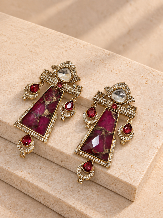 Shringara red trapezoid earrings with irregular gold-toned veining and red teardrop charms on beige square stones.