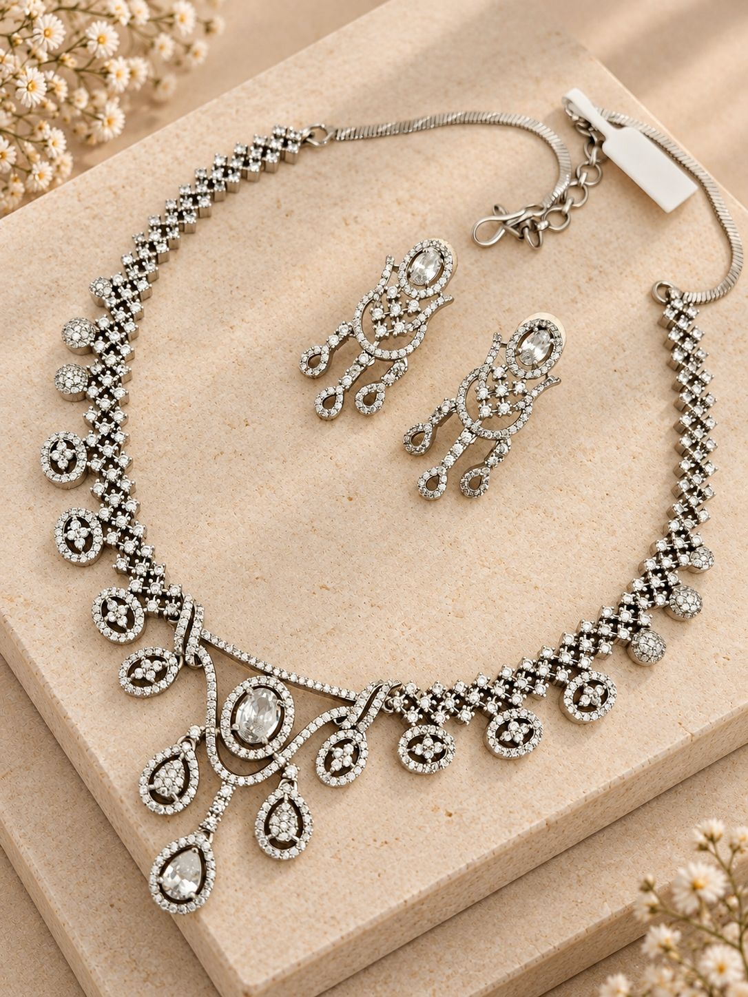 Silver-tone necklace with oval and teardrop clear-stone motifs and matching earrings on two beige square stones.