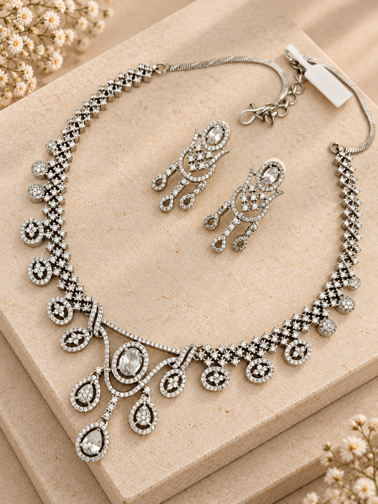 Silver-tone necklace with oval and teardrop clear-stone motifs and matching earrings on two beige square stones.