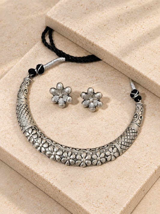 Silver-look floral Hasli necklace and matching flower studs with black cord resting on beige square stones.