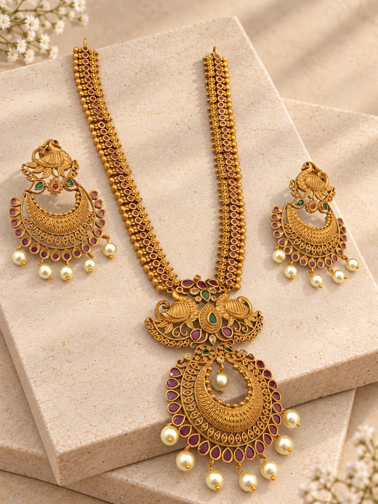 Matte gold-tone temple necklace and matching peacock earrings with red and green accents and pearl drops on beige square stones.