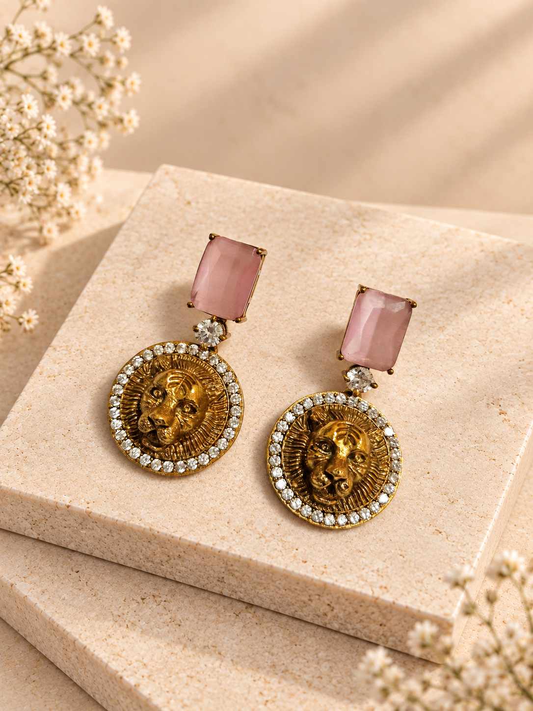 Antique gold-tone tiger head earrings with pink rectangular stones on beige square stone slabs